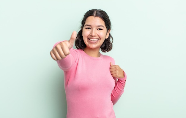 Mujer bonita adolescente que se siente orgullosa, despreocupada, segura y feliz, sonriendo positivamente con los pulgares hacia arriba