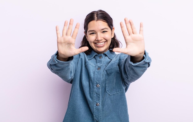 Mujer bonita adolescente sonriendo y mirando amistosamente, mostrando el número diez o décimo con la mano hacia adelante, contando hacia atrás