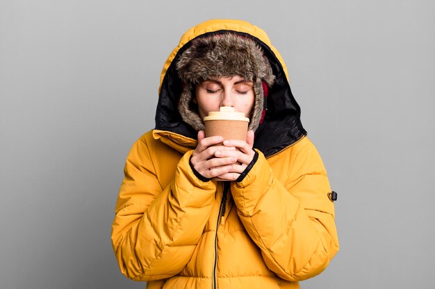 Mujer bonita adulta joven con anorak y sombrero de invierno y sosteniendo un café para llevar