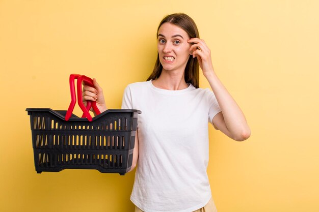 Mujer bonita adulta joven que sostiene una cesta de compras vacía