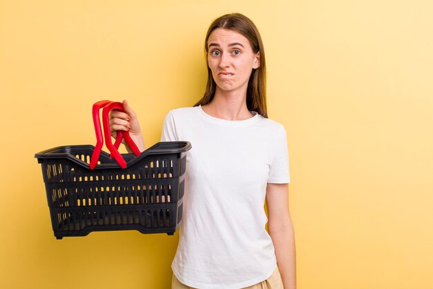 Mujer bonita adulta joven que sostiene una cesta de compras vacía