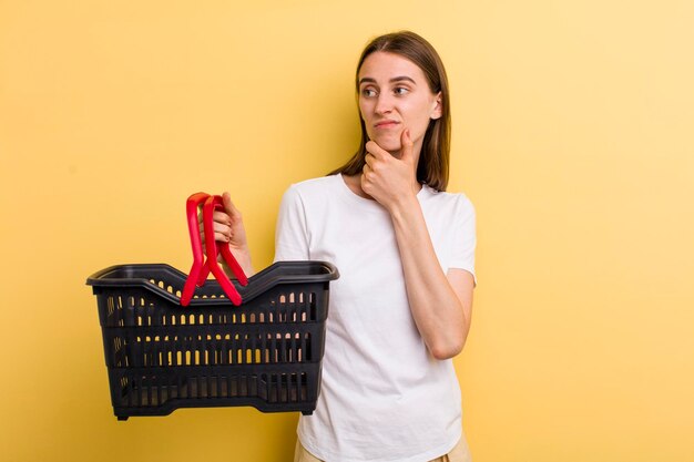 Mujer bonita adulta joven que sostiene una cesta de compras vacía