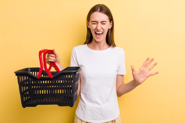 Mujer bonita adulta joven que sostiene una cesta de compras vacía