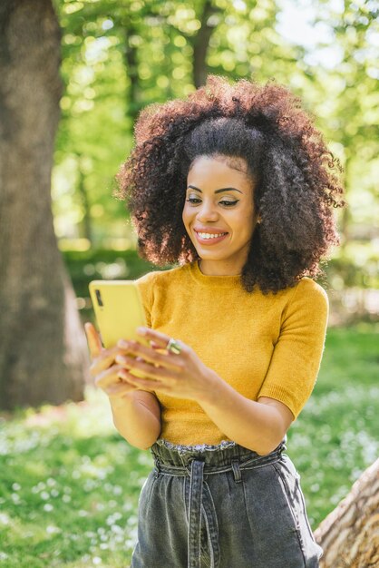 Mujer bonita afro escribiendo en el móvil, en el bosque. Enfoque selectivo.