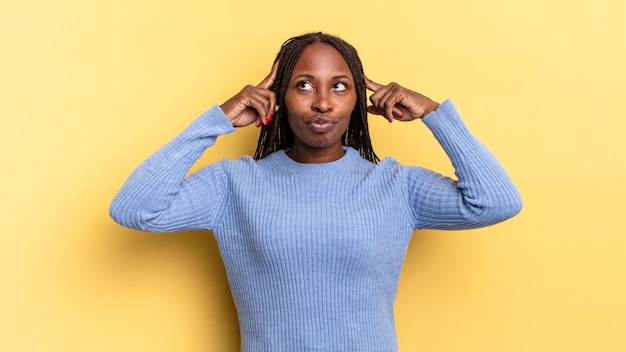 Mujer bonita afro negra que se siente confundida o dudando, concentrándose en una idea, pensando mucho, buscando copiar el espacio en el costado