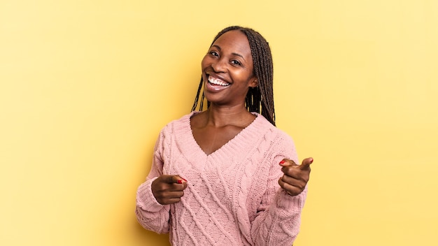 Mujer bonita afro negra que se siente feliz, fresca, satisfecha, relajada y exitosa, apuntando a la cámara, eligiéndote