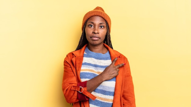 Mujer bonita afro negra que se siente feliz, positiva y exitosa, con la mano en forma de v sobre el pecho, mostrando victoria o paz