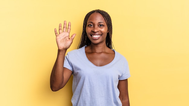 Mujer bonita afro negra sonriendo y mirando amigable, mostrando el número cinco o quinto con la mano hacia adelante, contando hacia atrás