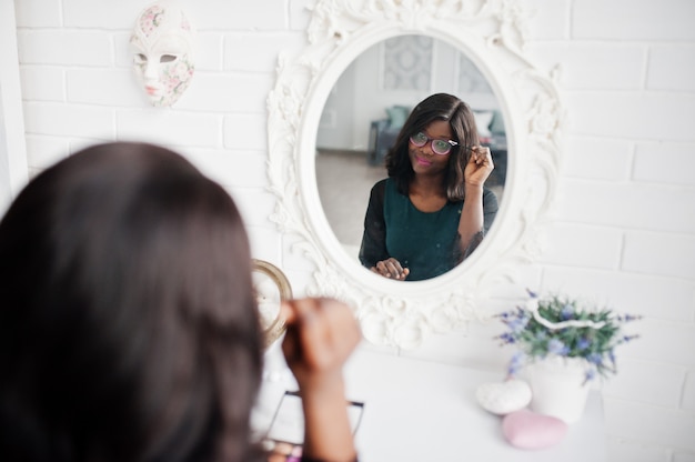 Mujer bonita afroamericana con paleta de maquillaje en las manos mirando el espejo.