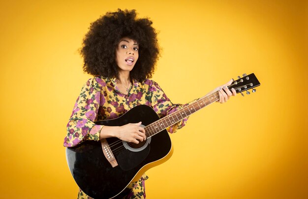 Mujer bonita alegre y popular con pelo afro tocando la guitarra aislado