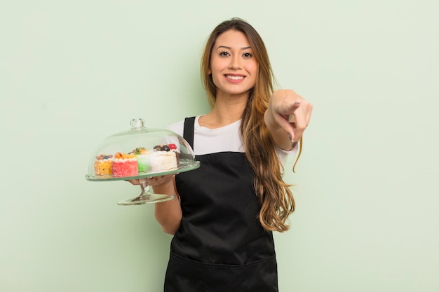 Mujer bonita asiática apuntando a la cámara eligiendo tu concepto de pasteles caseros