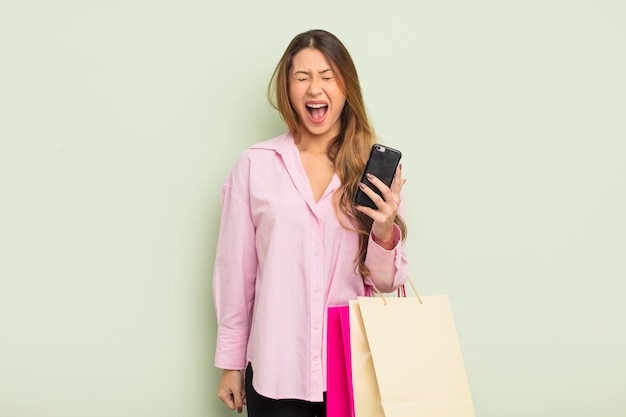 Mujer bonita asiática gritando agresivamente mirando el concepto de bolsas de compras muy enojada