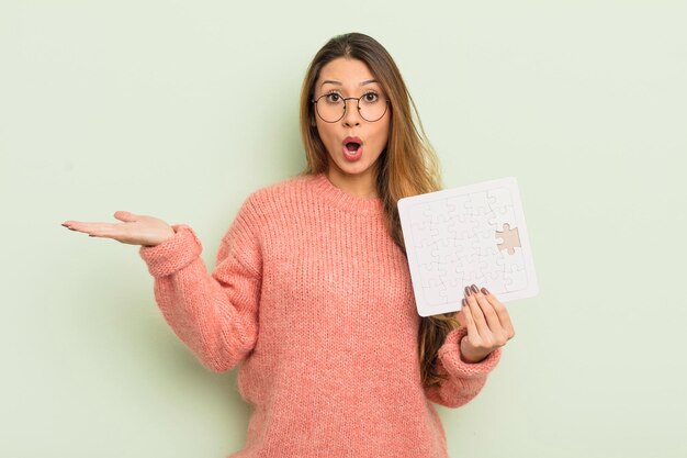 Mujer bonita asiática que parece sorprendida y conmocionada con la mandíbula caída sosteniendo un concepto de rompecabezas de objetos