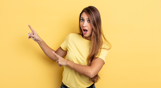 Mujer bonita asiática que se siente conmocionada y sorprendida, señalando el espacio de la copia en el costado con una mirada asombrada y con la boca abierta