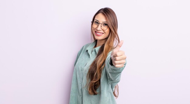 Mujer bonita asiática que se siente orgullosa, despreocupada, segura y feliz, sonriendo positivamente con los pulgares hacia arriba