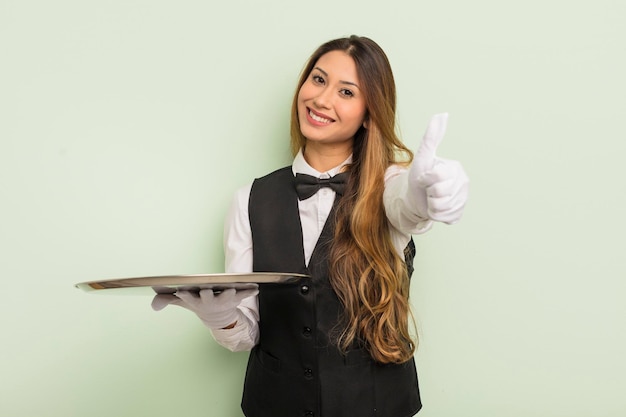 Mujer bonita asiática que se siente orgullosa, sonriendo positivamente con los pulgares hacia arriba. concepto de camarero y bandeja