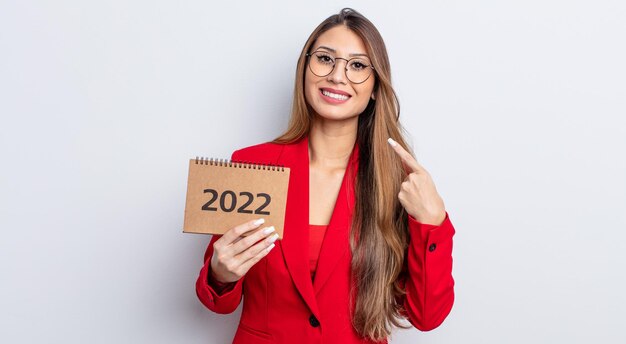 Mujer bonita asiática sonriendo con confianza apuntando a su propia amplia sonrisa. concepto de calendario