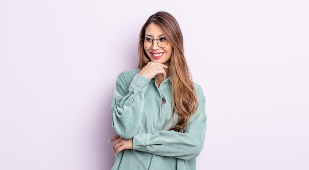 Mujer bonita asiática sonriendo con una expresión feliz y segura con la mano en la barbilla, preguntándose y mirando hacia un lado