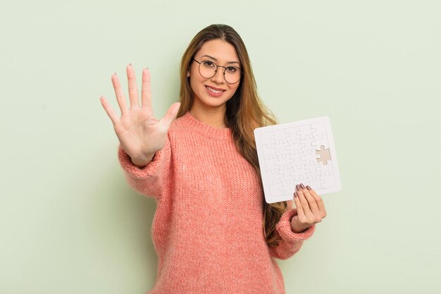 Mujer bonita asiática sonriendo y luciendo amigable mostrando el concepto de rompecabezas número cinco