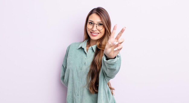 Mujer bonita asiática sonriendo y luciendo feliz, despreocupada y positiva, gesticulando victoria o paz con una mano