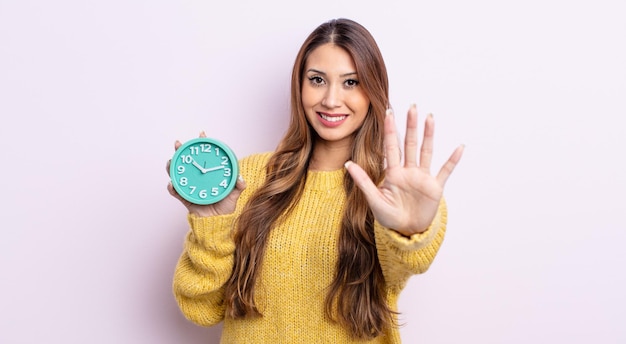 Mujer bonita asiática sonriendo y mirando amigable, mostrando el número cinco. concepto de reloj despertador