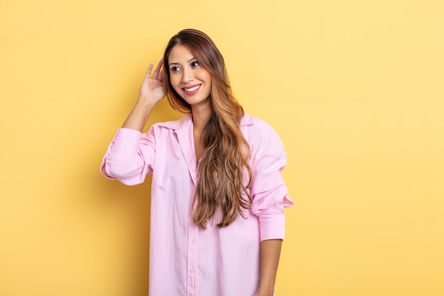 Mujer bonita asiática sonriendo, mirando curiosamente a un lado, tratando de escuchar chismes o escuchando un secreto