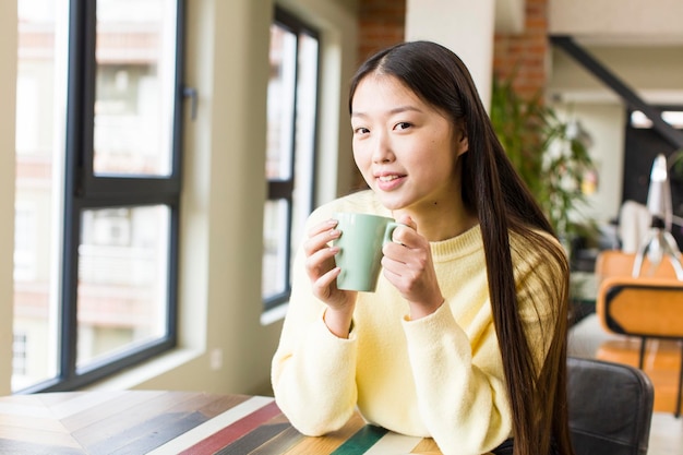 Mujer bonita asiática con una taza de café en casa fresca