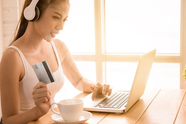 Mujer bonita con auriculares con tarjeta de crédito y usando la computadora portátil