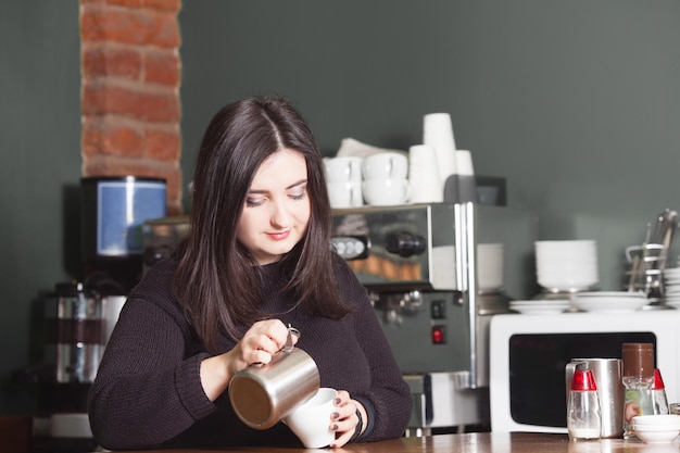 Mujer bonita barista haciendo capuchino. Verter leche y espuma en una taza.