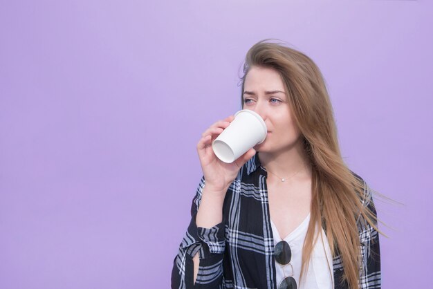 La mujer bonita bebe una bebida de un vidrio blanco blanco en un fondo púrpura.