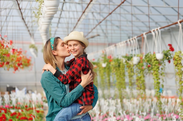 Mujer bonita besando y abrazando encantadora hija niño en el invernadero feliz familia jardinero