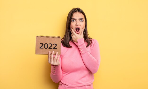 Mujer bonita con la boca y los ojos bien abiertos y la mano en la barbilla. Concepto de calendario 2022