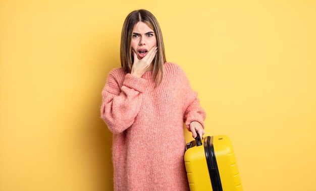 Mujer bonita con la boca y los ojos bien abiertos y la mano en la barbilla. concepto de viaje de maleta