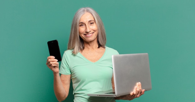 Mujer bonita de cabello gris con un celular y una computadora portátil