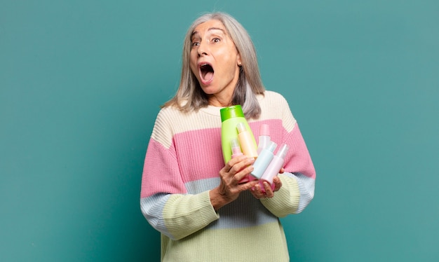 Mujer bonita de cabello gris con productos para el cuidado de la piel