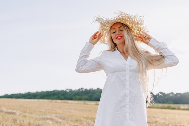 Mujer bonita con cabello largo rubio en un sombrero de paja en un campo al atardecer. verano, agricultura, naturaleza y aire fresco.