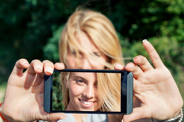 Foto una mujer bonita con cabello rubio se hace una selfie con su teléfono inteligente.