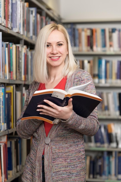 Mujer bonita con cabello rubio de pie en la biblioteca Libros borrosos en la parte posterior