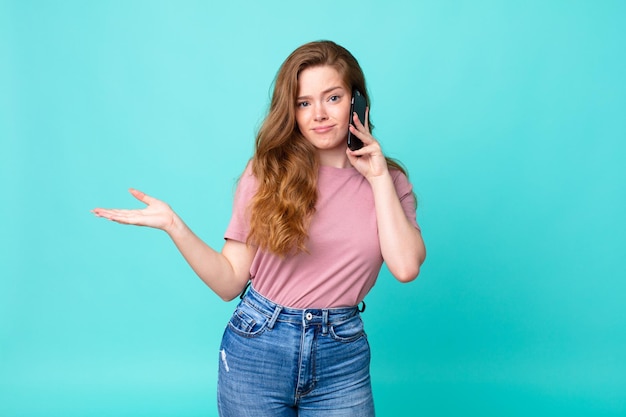 Foto mujer bonita cabeza roja que se siente desconcertada y confundida y dudando y usando un teléfono inteligente