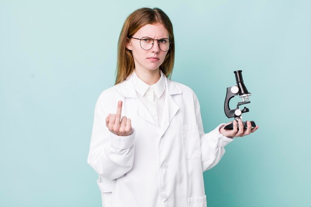 Mujer bonita de cabeza roja que se siente enojada, científica rebelde y agresiva con el concepto de microscopio