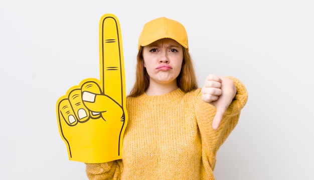 Mujer bonita de cabeza roja que se siente mostrando los pulgares hacia abajo el concepto de ventilador de mano número uno