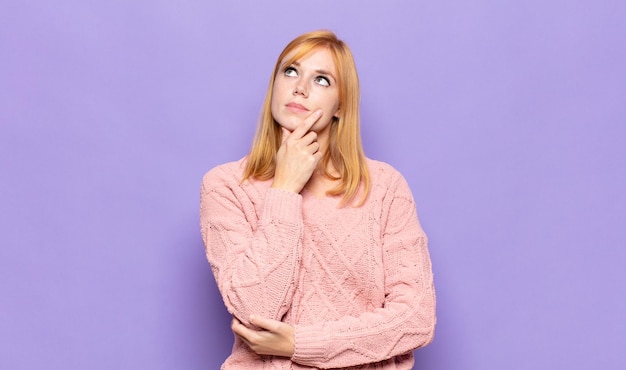 Mujer bonita cabeza roja que se siente pensativa, preguntándose o imaginando ideas, soñando despierto y mirando hacia arriba para copiar el espacio