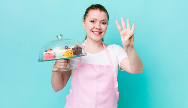 Mujer bonita de cabeza roja sonriendo y luciendo amigable mostrando el concepto de pasteles caseros número cuatro