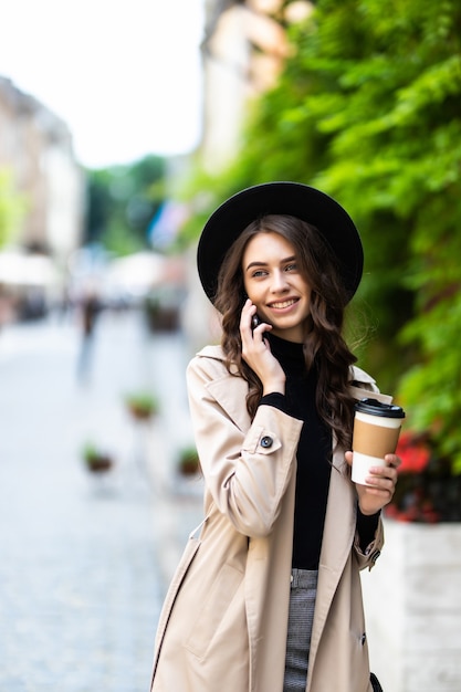 Mujer bonita caminando y hablando con teléfonos inteligentes en la calle en un día soleado de verano