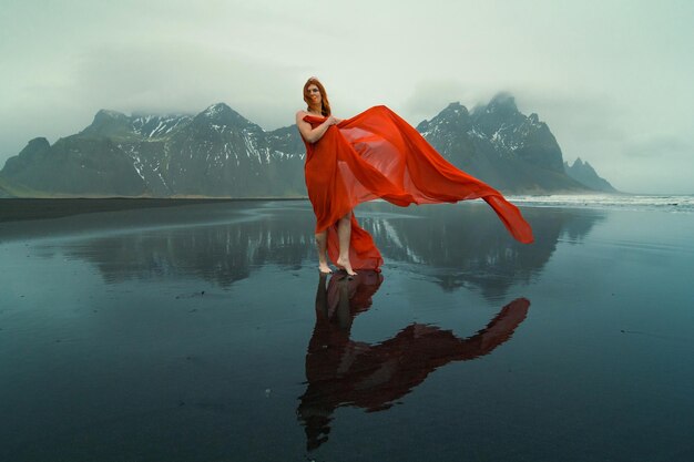 Mujer bonita con capa ondeante en la fotografía escénica de la playa de Reynisfjara