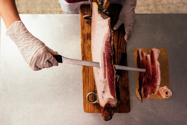 Mujer bonita carnicería cortando jamón con cuchillo.