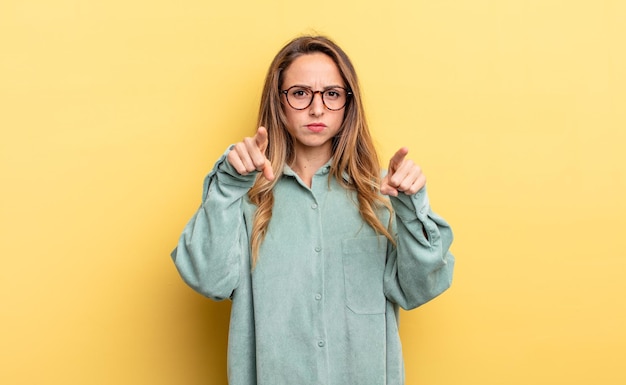 Mujer bonita caucásica apuntando hacia la cámara con ambos dedos y expresión enojada, diciéndole que cumpla con su deber