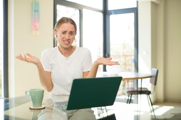 Mujer bonita caucásica con una computadora portátil que parece perpleja, confundida y estresada, preguntándose entre diferentes opciones, sintiéndose insegura