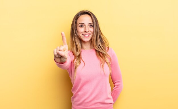 Mujer bonita caucásica sonriendo con orgullo y confianza haciendo la pose número uno triunfalmente, sintiéndose como un líder