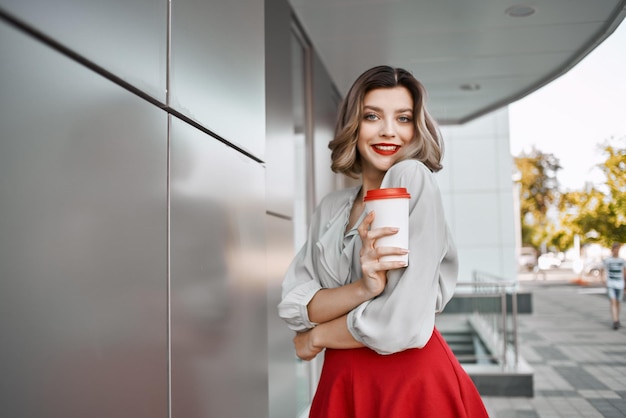 Mujer bonita cerca de edificio con taza de café posando estilo de vida de moda
